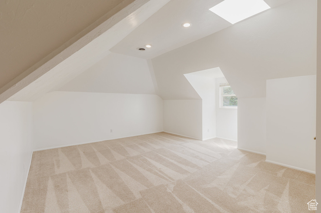 Additional living space featuring light colored carpet and vaulted ceiling with skylight