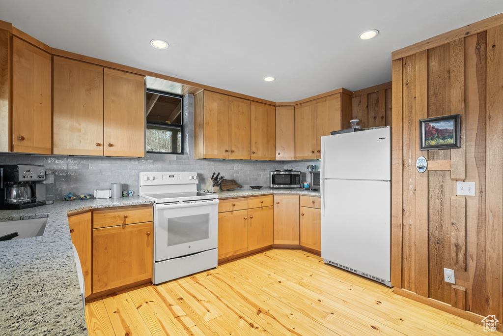 Kitchen with white appliances, tasteful backsplash, light wood-type flooring, and light stone countertops