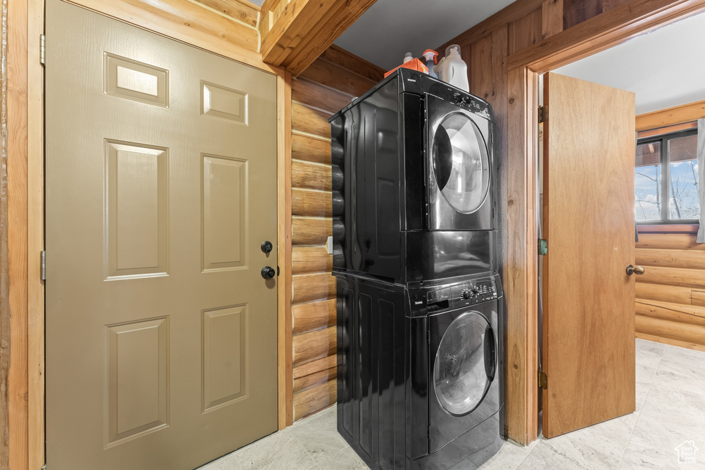 Laundry area featuring light tile floors, stacked washer / drying machine, and rustic walls