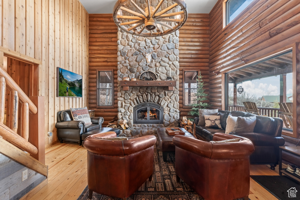 Living room featuring hardwood / wood-style floors, log walls, a stone fireplace, and a towering ceiling