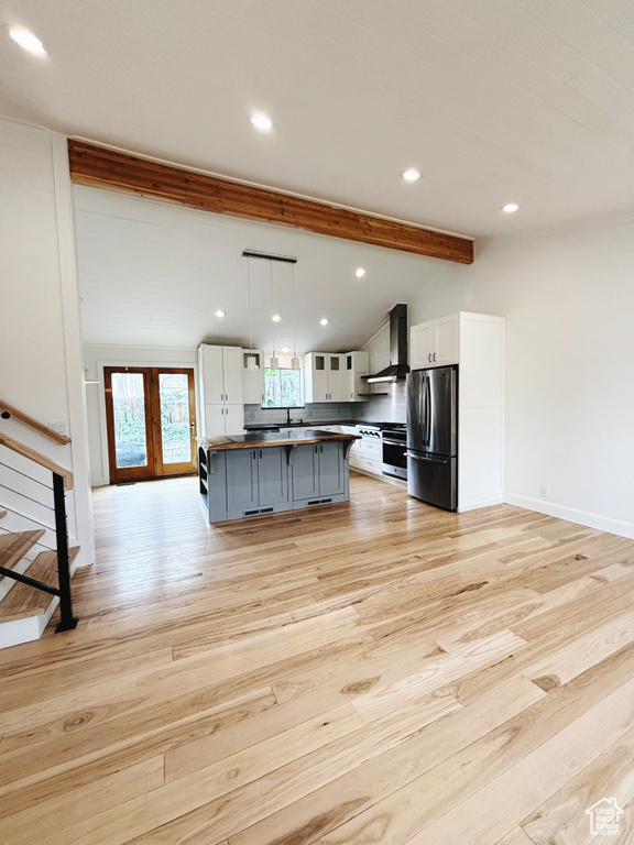 Kitchen featuring a center island, decorative light fixtures, light hardwood / wood-style flooring, wall chimney range hood, and stainless steel fridge