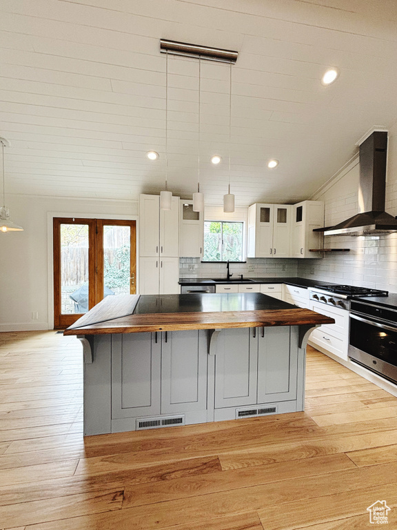 Kitchen with butcher block counters, hanging light fixtures, tasteful backsplash, wall chimney exhaust hood, and light wood-type flooring