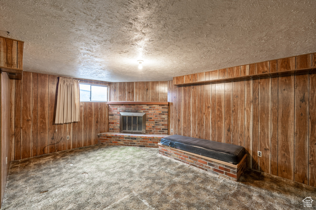 Basement with wood walls, a brick fireplace, carpet floors, and a textured ceiling