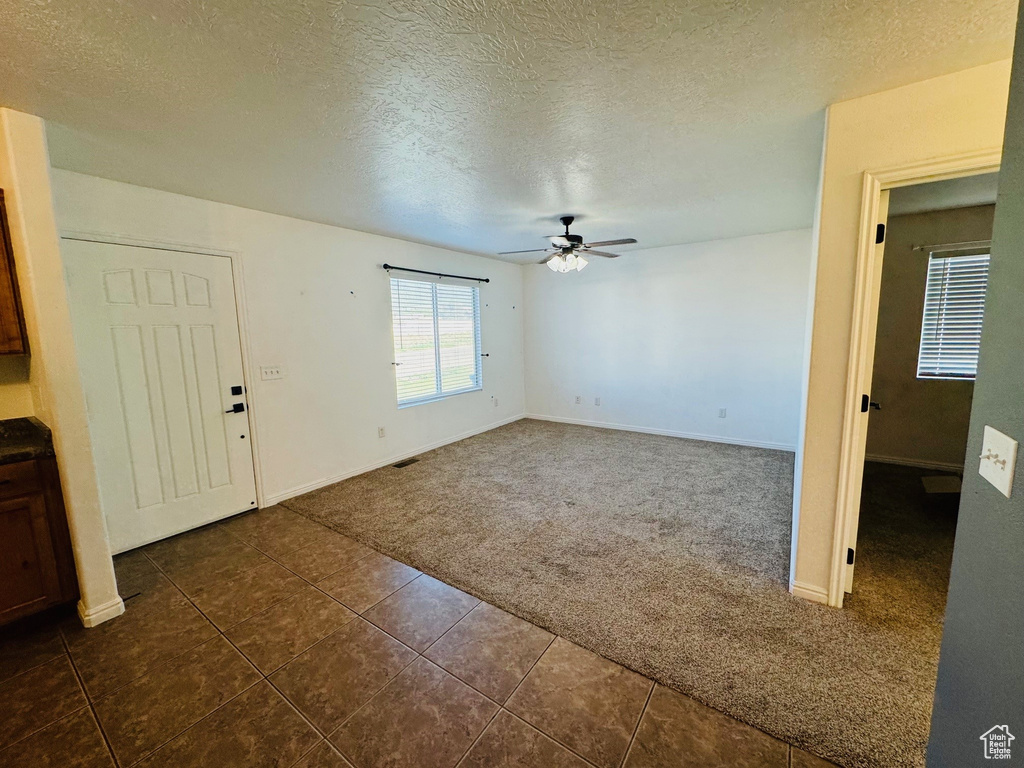Empty room with ceiling fan, dark tile floors, and a textured ceiling