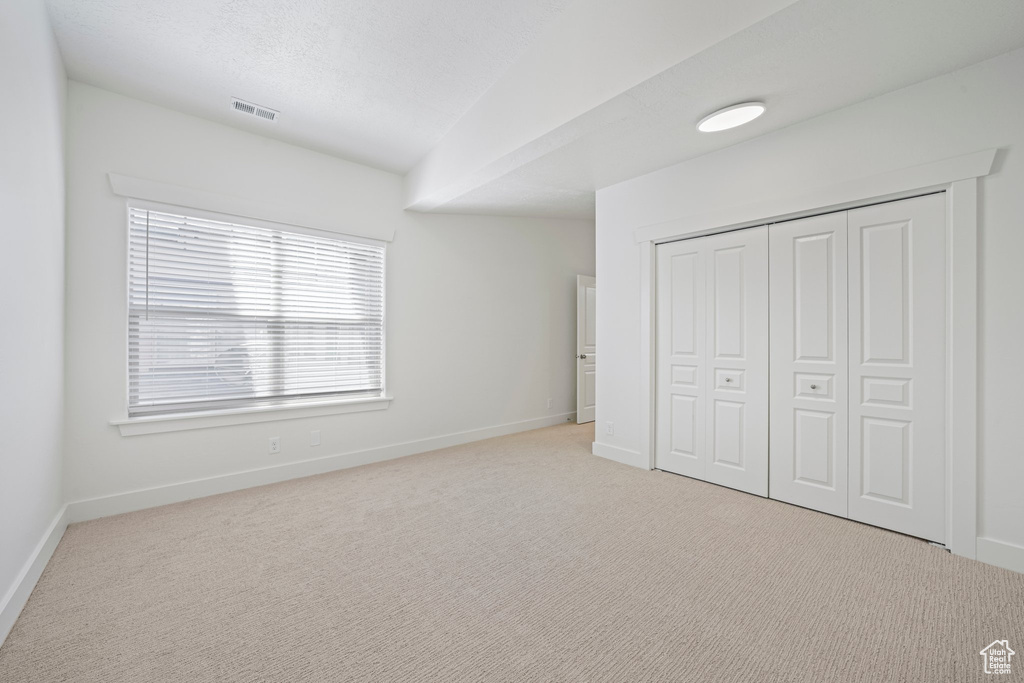 Unfurnished bedroom with light colored carpet, a closet, and multiple windows