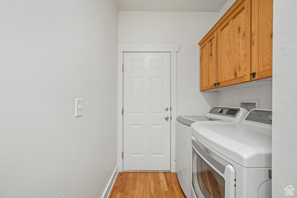 Washroom featuring light hardwood / wood-style floors, cabinets, and washing machine and clothes dryer