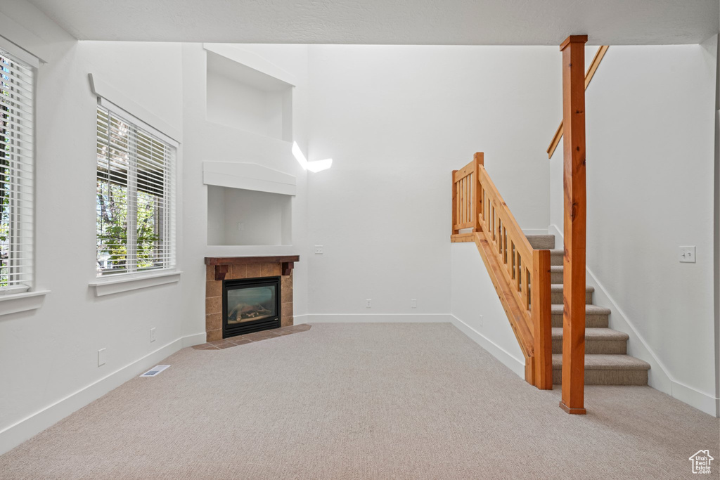 Unfurnished living room featuring carpet flooring and a tiled fireplace