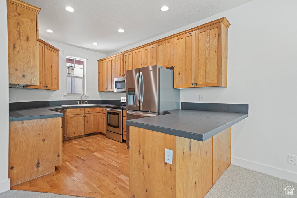 Kitchen with sink, appliances with stainless steel finishes, kitchen peninsula, and light wood-type flooring