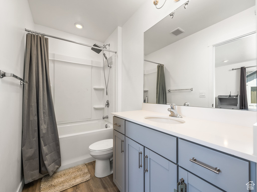Full bathroom with hardwood / wood-style floors, shower / bath combination with curtain, toilet, and vanity