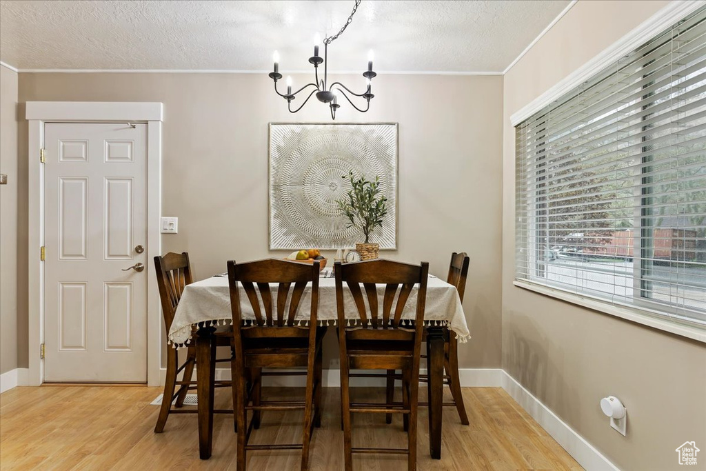 Dining space featuring light hardwood / wood-style floors, a chandelier, crown molding, and a textured ceiling