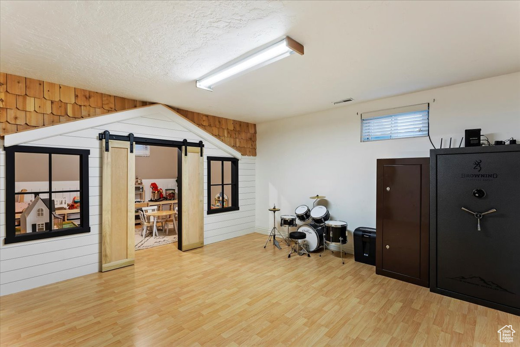 Miscellaneous room featuring wood walls, a barn door, light hardwood / wood-style floors, and a textured ceiling