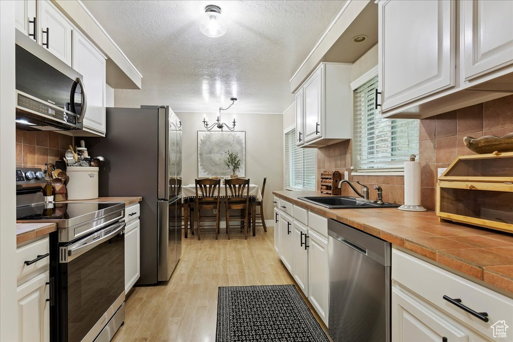 Kitchen with appliances with stainless steel finishes, backsplash, light hardwood / wood-style floors, white cabinetry, and sink