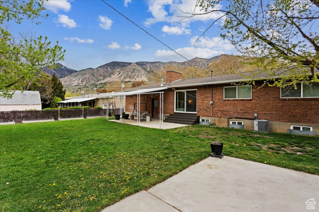 Back of property with a patio area, a mountain view, a lawn, and central AC unit