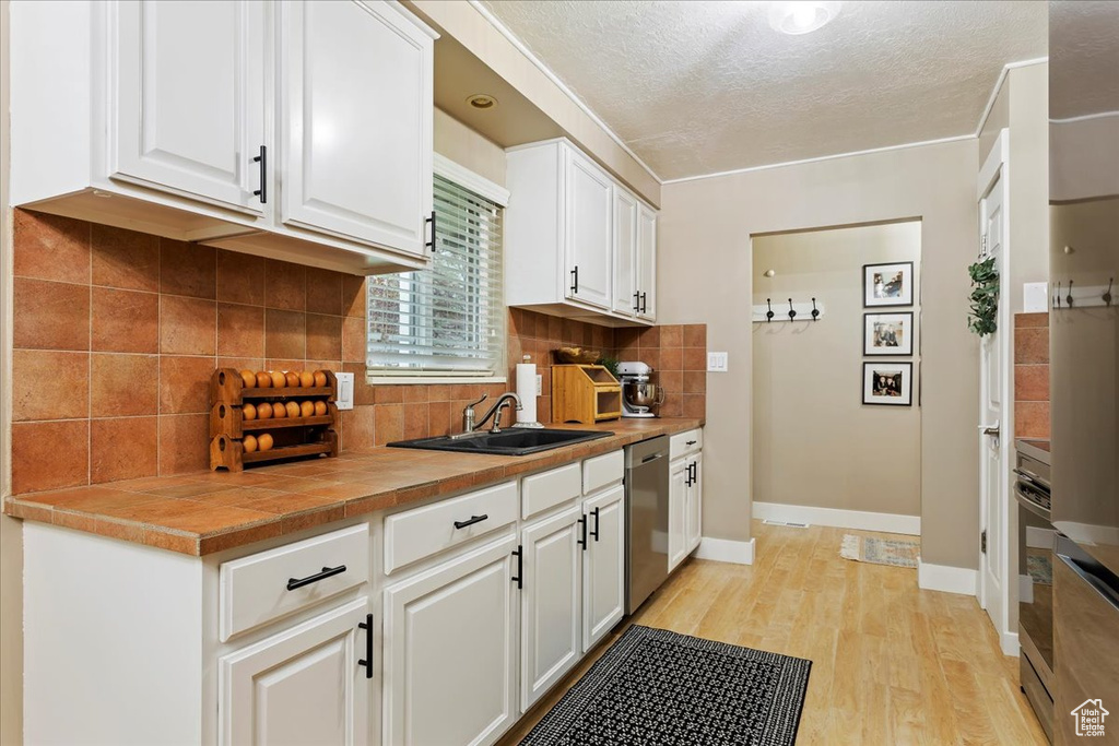 Kitchen featuring sink, light hardwood / wood-style floors, tasteful backsplash, and white cabinetry