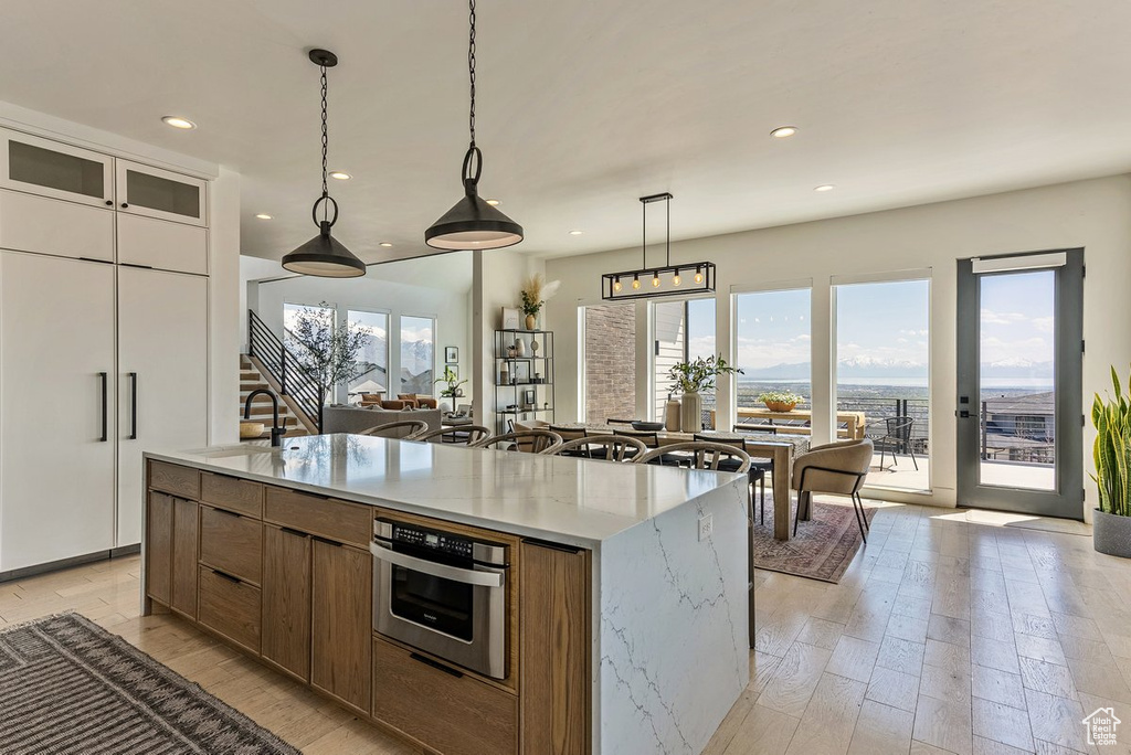 Kitchen featuring pendant lighting, stainless steel oven, light stone counters, light hardwood / wood-style floors, and an island with sink