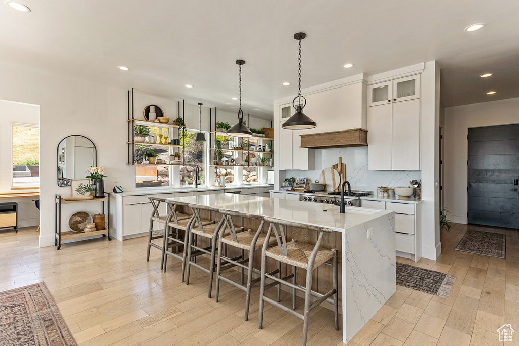 Kitchen featuring decorative light fixtures, light hardwood / wood-style floors, a large island, custom exhaust hood, and white cabinetry