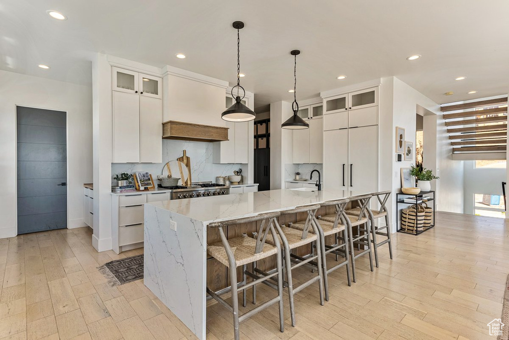 Kitchen with stove, hanging light fixtures, white cabinets, a large island, and backsplash