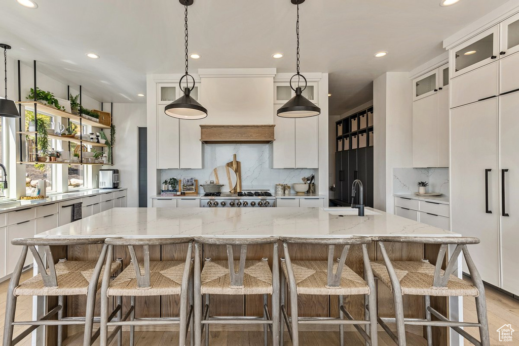 Kitchen featuring tasteful backsplash, white cabinetry, a center island with sink, and light wood-type flooring