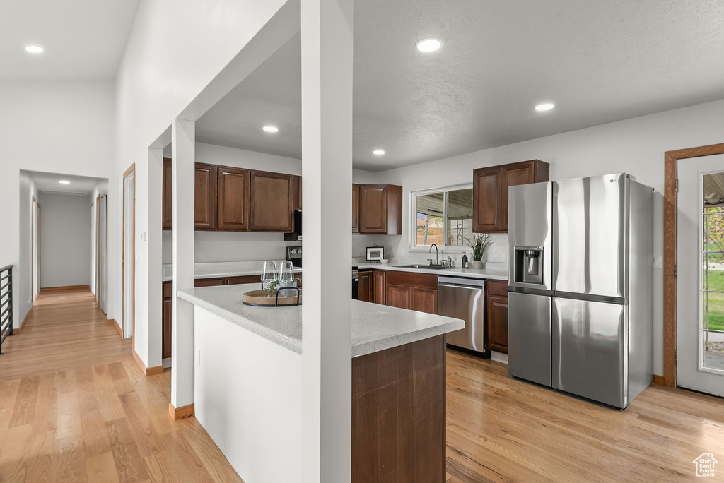 Kitchen featuring appliances with stainless steel finishes, dark brown cabinetry, sink, and light hardwood / wood-style floors
