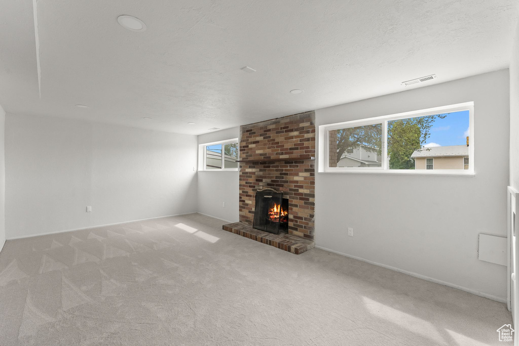 Unfurnished living room featuring light colored carpet, brick wall, a healthy amount of sunlight, and a fireplace