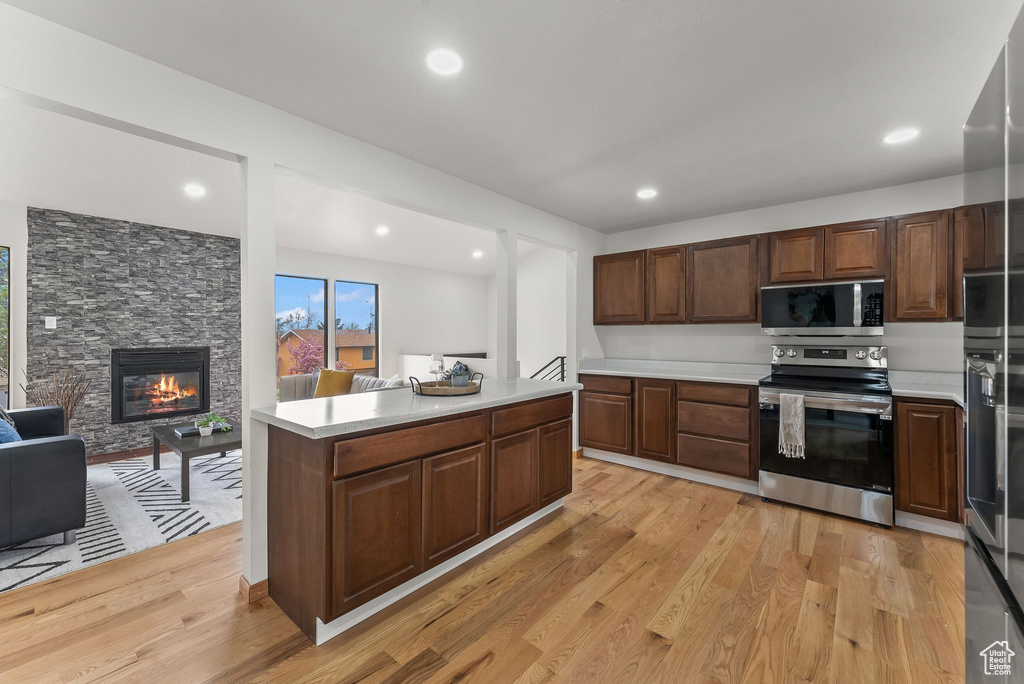 Kitchen featuring light hardwood / wood-style floors, stainless steel appliances, dark brown cabinetry, and a fireplace