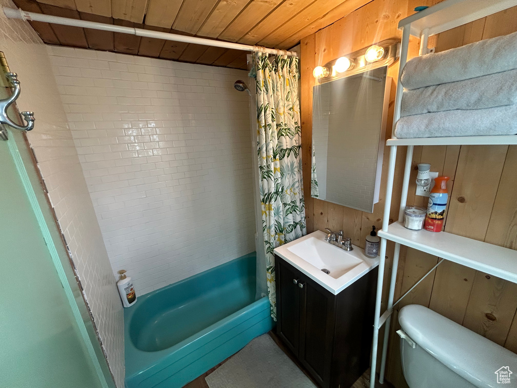 Full bathroom featuring wood walls, shower / bath combination with curtain, toilet, vanity, and wooden ceiling