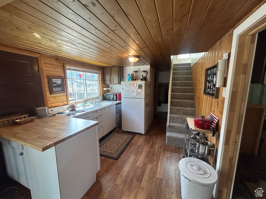 Kitchen with white fridge, dark hardwood / wood-style floors, wood ceiling, and wooden walls
