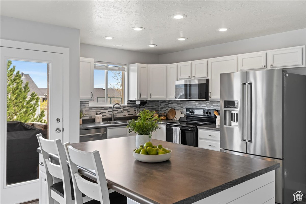 Kitchen with backsplash, appliances with stainless steel finishes, white cabinets, and sink