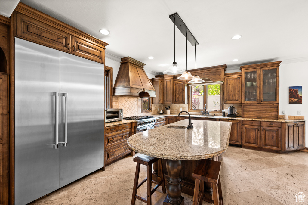 Kitchen with pendant lighting, premium appliances, backsplash, custom range hood, and light stone counters