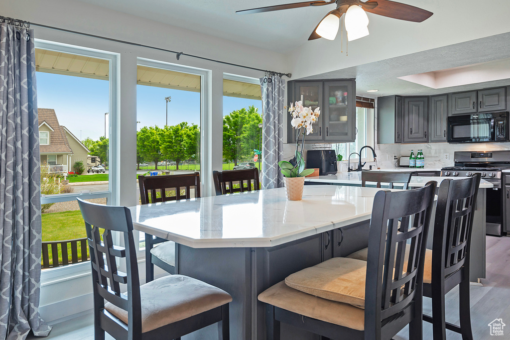 Kitchen featuring backsplash, gas stove, ceiling fan, hardwood / wood-style flooring, and gray cabinetry