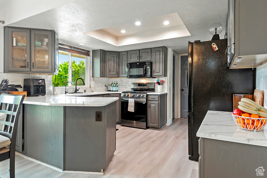 Kitchen with kitchen peninsula, light hardwood / wood-style floors, black appliances, and a tray ceiling
