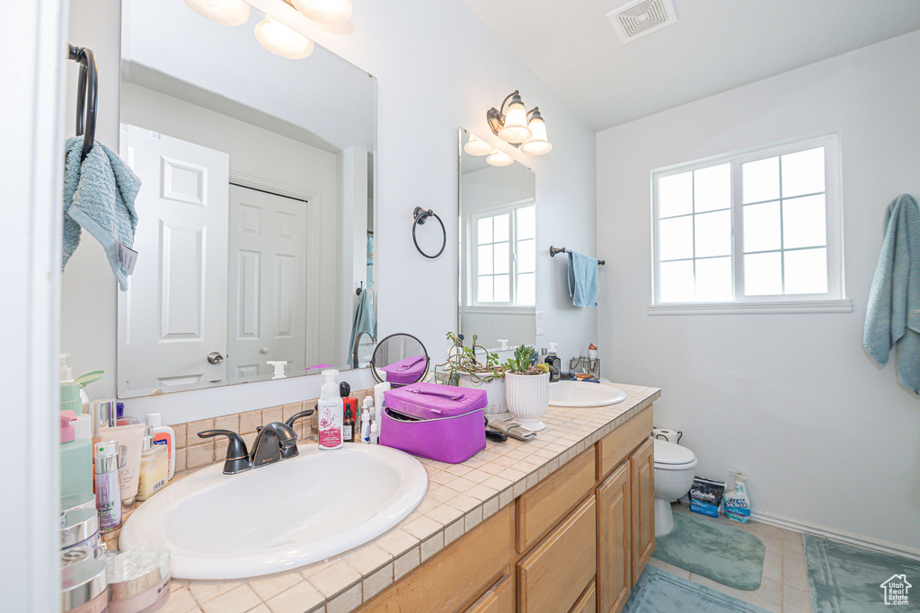 Bathroom with dual bowl vanity, toilet, and tile flooring