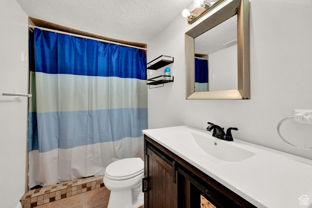 Bathroom with tile flooring, vanity, toilet, and a textured ceiling