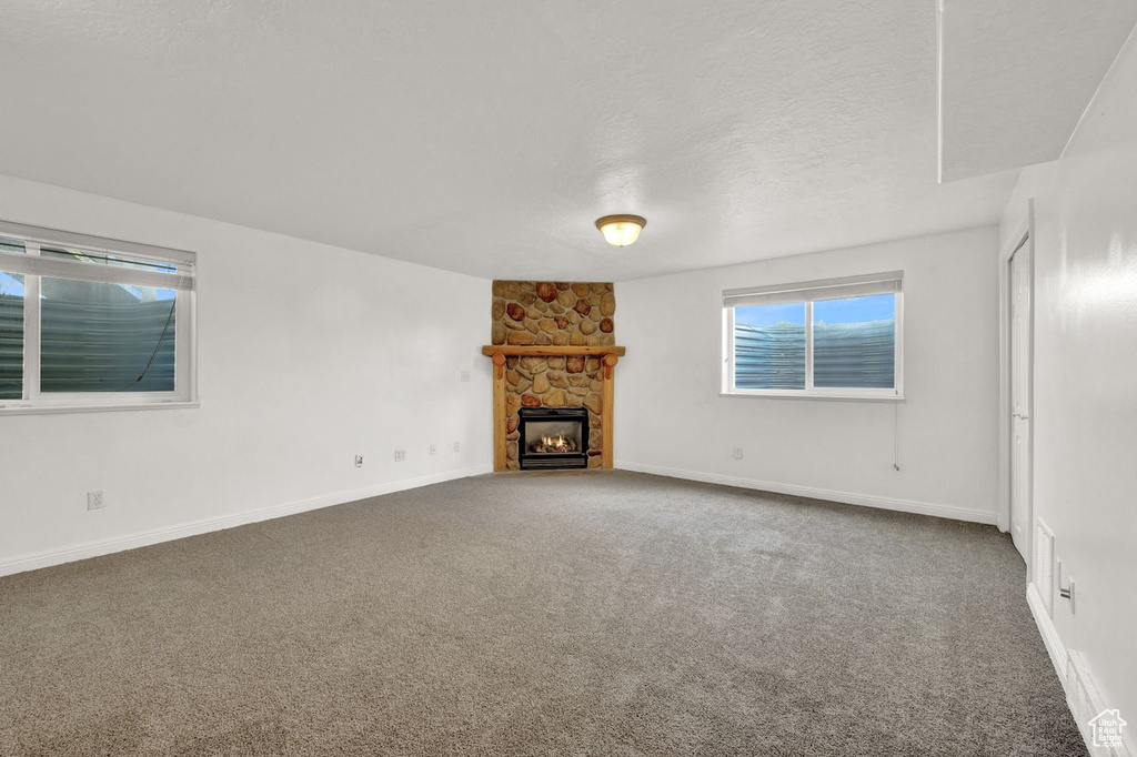 Unfurnished living room with carpet, a stone fireplace, and a textured ceiling
