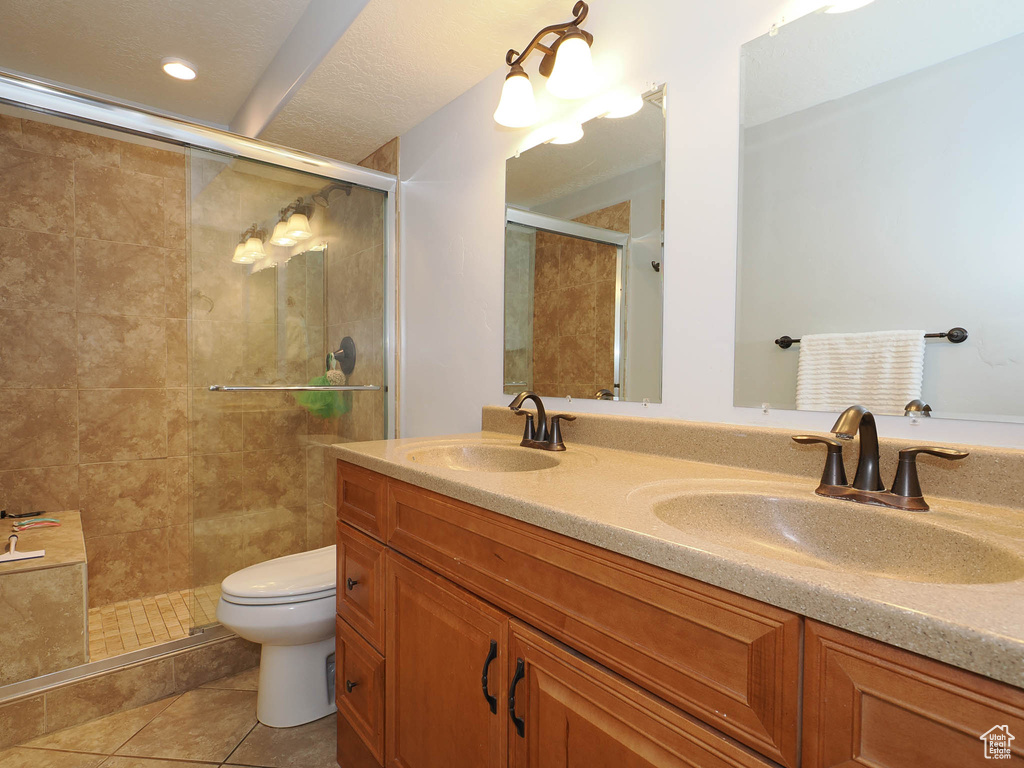 Bathroom featuring a shower with shower door, toilet, tile flooring, a textured ceiling, and dual vanity