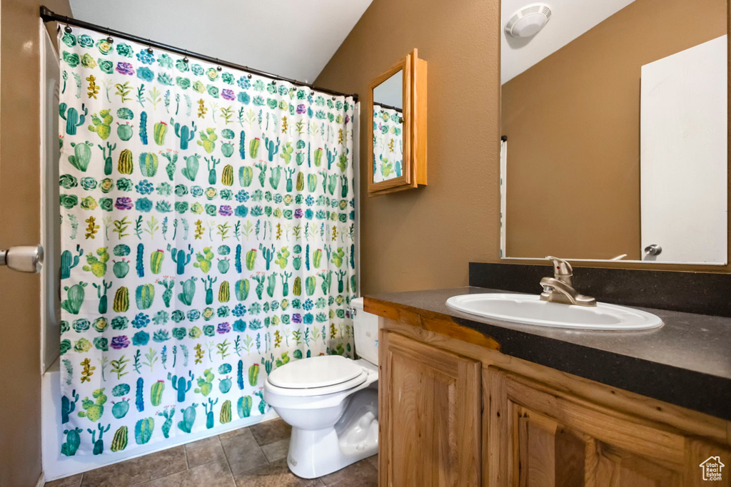 Bathroom featuring tile flooring, vaulted ceiling, vanity, and toilet