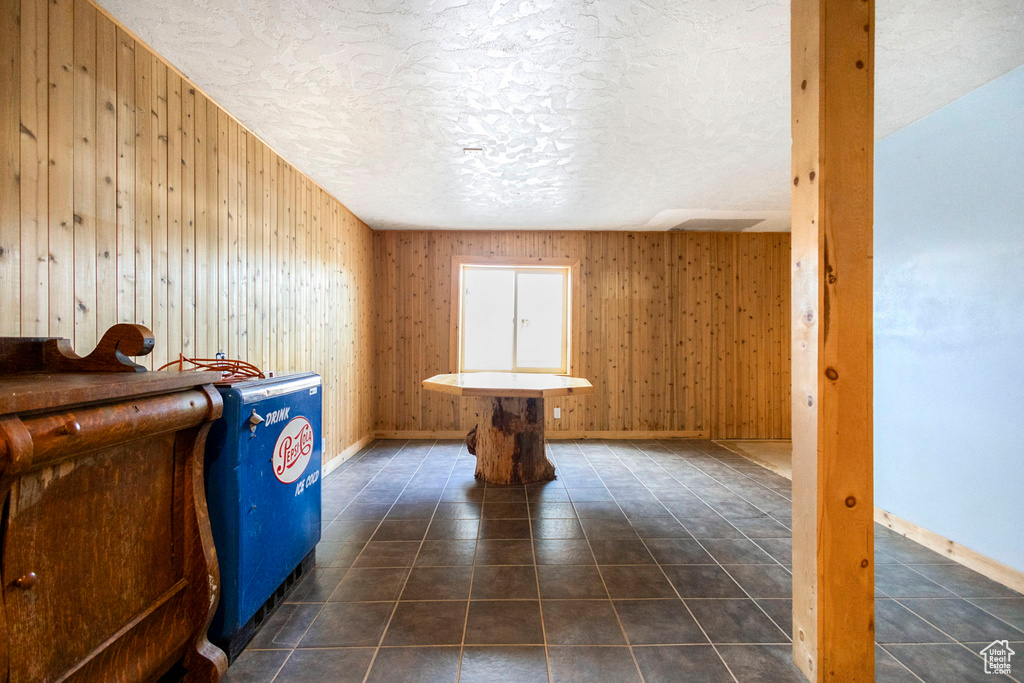 Interior space featuring a textured ceiling, dark tile flooring, and wooden walls