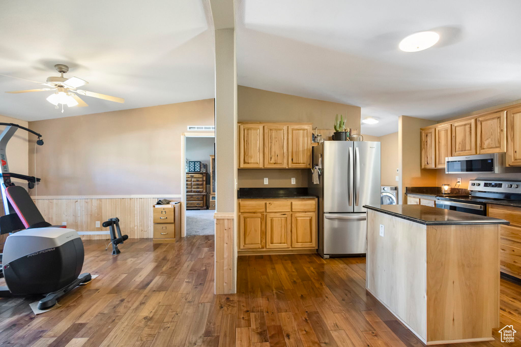 Kitchen with vaulted ceiling, stainless steel appliances, ceiling fan, washer / dryer, and wood-type flooring