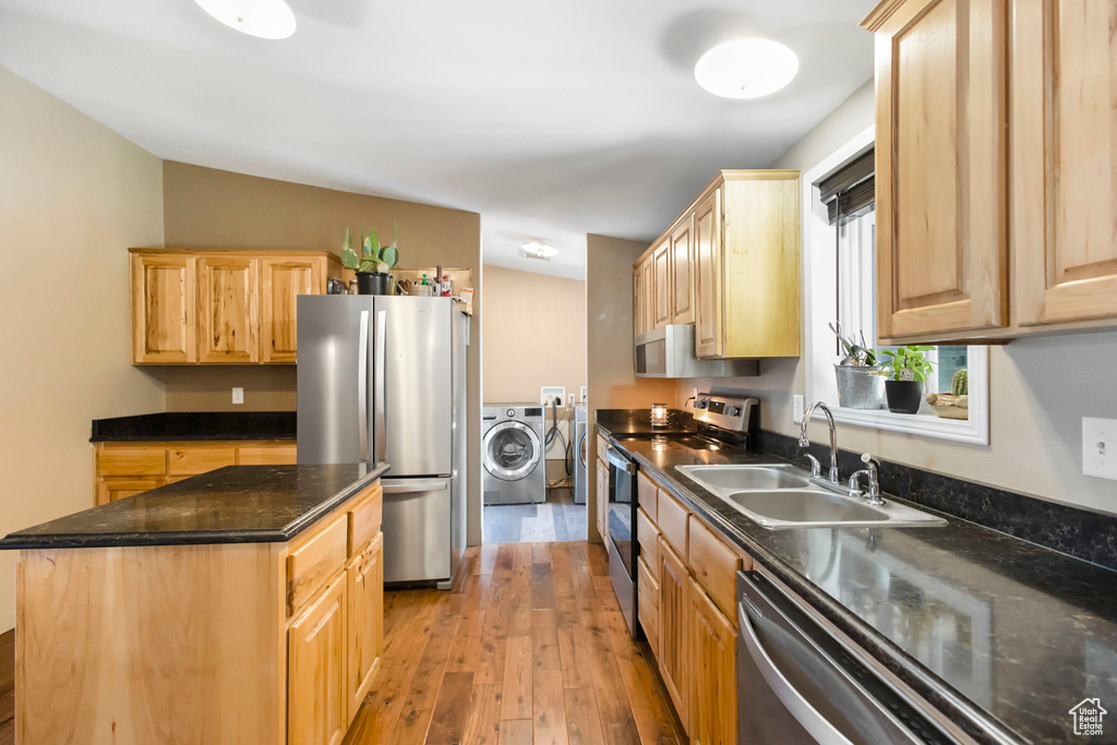 Kitchen featuring appliances with stainless steel finishes, a center island, sink, washer / clothes dryer, and light hardwood / wood-style flooring