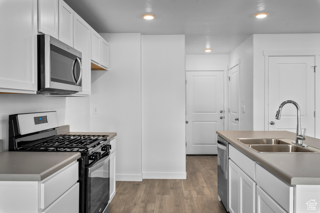 Kitchen featuring appliances with stainless steel finishes, hardwood / wood-style flooring, a kitchen island with sink, white cabinets, and sink