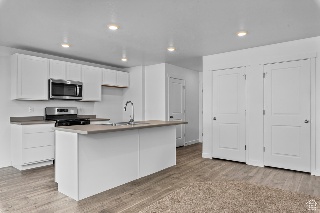 Kitchen with appliances with stainless steel finishes, hardwood / wood-style floors, a center island with sink, and sink
