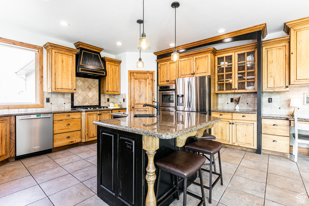 Kitchen featuring backsplash, appliances with stainless steel finishes, light tile floors, and a center island with sink