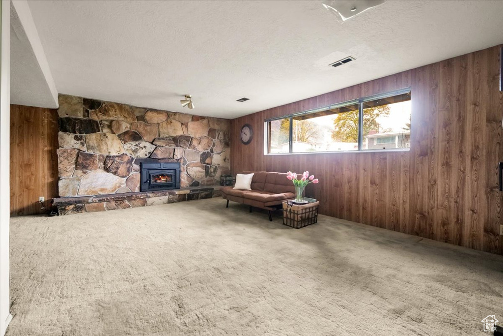 Unfurnished room featuring wood walls, carpet, and a stone fireplace