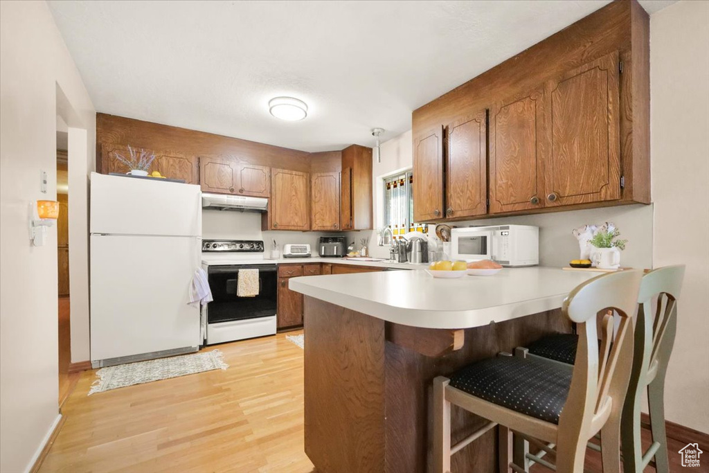 Kitchen with a kitchen breakfast bar, white appliances, light hardwood / wood-style flooring, kitchen peninsula, and sink