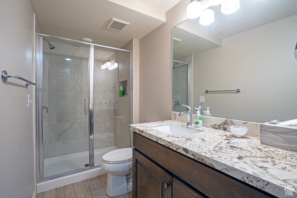 Bathroom with a textured ceiling, oversized vanity, a shower with shower door, and toilet