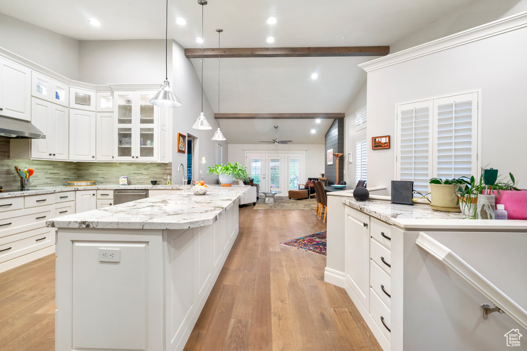 Kitchen with beamed ceiling, white cabinets, tasteful backsplash, light wood-type flooring, and pendant lighting