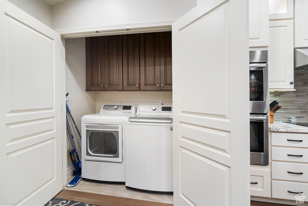 Laundry area with light hardwood / wood-style flooring, cabinets, and washing machine and clothes dryer