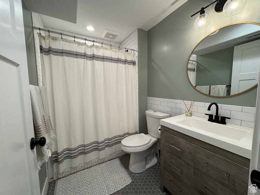 Bathroom with tile walls, large vanity, toilet, tile flooring, and tasteful backsplash