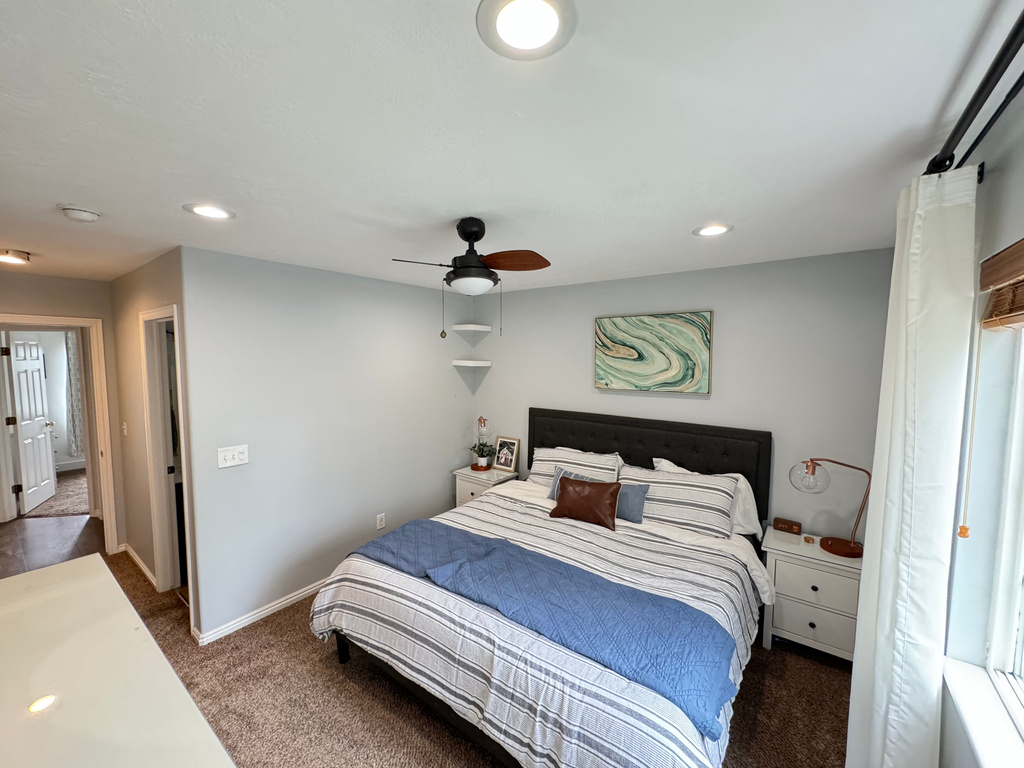 Carpeted bedroom featuring ceiling fan and multiple windows