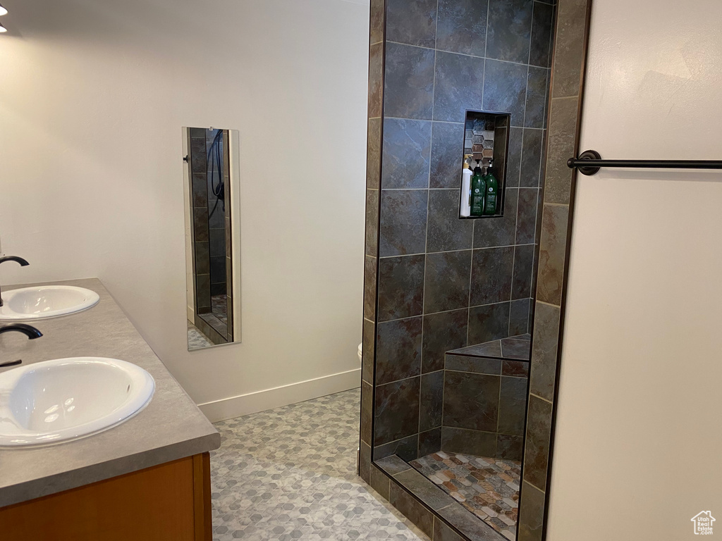 Bathroom with dual bowl vanity, tile flooring, and a tile shower